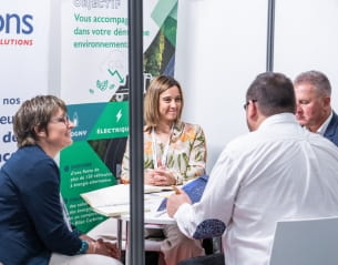 Réunion dans un stand de Top Transport Europe avec une affiche sur les initiatives environnementales.