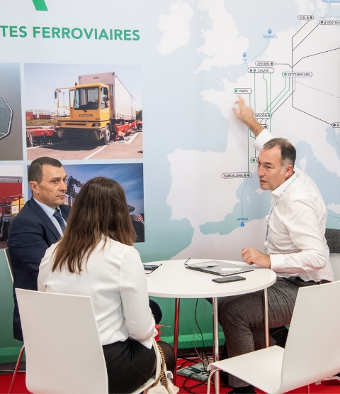 Three people talking in front of a map of rail routes at Top Transport Europe.